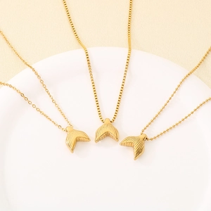 Golden fishtail pendant necklaces with box, cross, and bead chains on a white tray