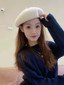Detailed view of a thick white wool beret paired with a blue cable knit sweater