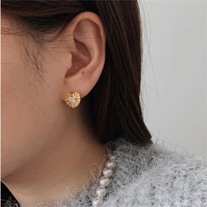 Detailed view of gold heart earrings with wrinkled texture and zircon on a model