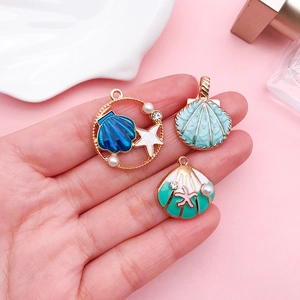 Trois pendentifs en forme de coquillage coloré avec perles sur un fond rose doux