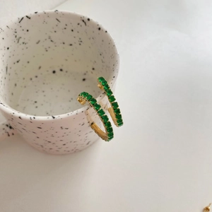 Gold hoop earrings with rectangular green zircons displayed on a ceramic cup edge