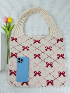 Flat lay of cream knit tote bag with red bows and smartphone for size reference