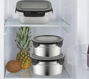 Three stainless steel food containers with black lids stored inside a refrigerator
