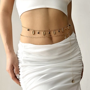 Detail of a gold-layered waist chain with shell pendants and black beads on white clothing