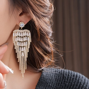 Close-up of long gold fringe earrings with clear zircons worn by a model in a luxury style