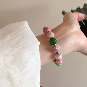 Detail of beaded bracelet with gold plating, pink floral beads and a green accent stone