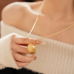 Collier avec pendentif ovale brossé plaqué or et chaîne serpent sur tricot blanc