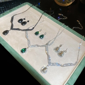 Detail view of teardrop necklace and earring sets in emerald green and clear diamond styles