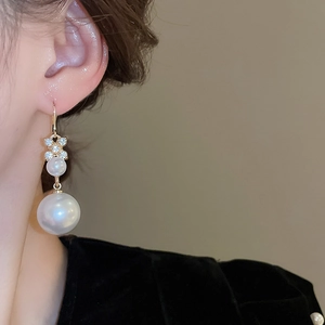 Dettaglio di orecchini a quadrifoglio dorati con strass e doppie perle indossati da modella