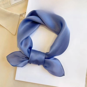 Minimalist solid blue square silk scarf elegantly tied on a book and beige shirt