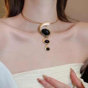 Close-up of gold collar necklace with spiral black resin pendant worn by model