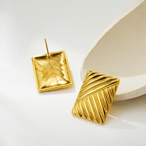 Macro view of gold plated rectangular earrings featuring textured diagonal stripes