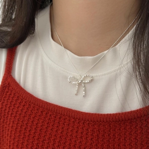 Detail of silver bow pendant necklace with rectangle metal blocks worn over red cardigan