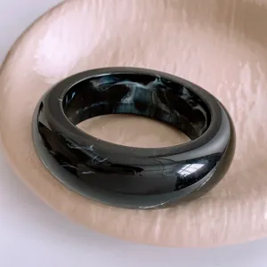 Minimalist black resin bangle with white marble texture on a decorative plate
