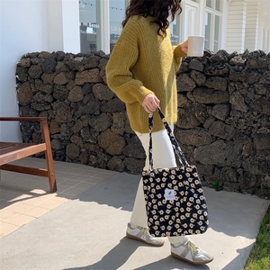 Corduroy snap tote bag in black floral pattern styled with a yellow knit sweater