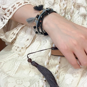 Detail of bohemian multilayer beaded bracelet with black and grey tassels on woman's wrist