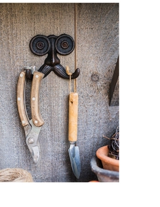 Detail van vintage gietijzeren snor wandhaak op rustiek hout met tuingereedschap