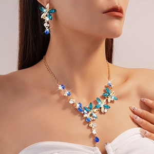 Close-up of golden floral necklace and earrings set with blue crystals on a model