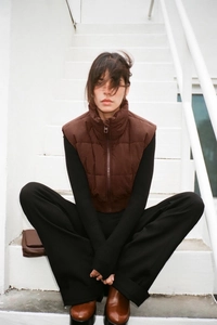 Detail of a brown stand-collar puffer vest showing quilted fabric and a smooth zipper design