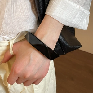 Polished black resin geometric bangle with irregular facets worn on a model's wrist