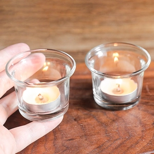 Minimalist clear glass tea light candle holder with lit wax candle on warm wood background