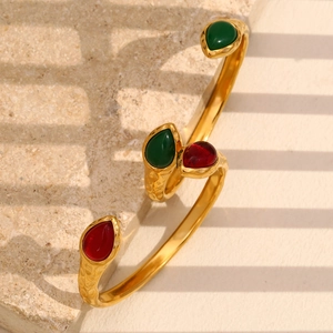 Close-up of snake head gold bangle with red and green gems on a textured beige stone surface