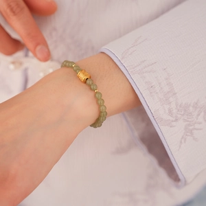 Detailed shot of green beads bracelet with a gold carved fortune bead on wrist