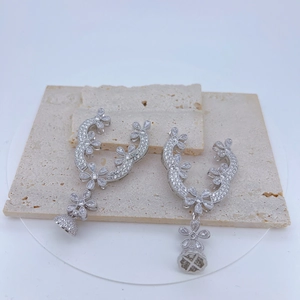 Detail of silver floral earrings with zircons and spherical pendants on stones