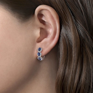 Close-up of elegant silver hoop earrings with three pear-shaped blue stones on ear