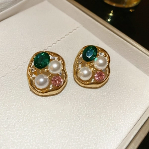 Detailed close-up of retro gold irregular earrings with green stones and pearls in jewelry box