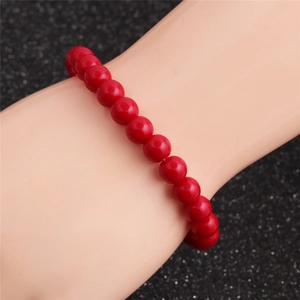 Détail d'un bracelet en perles rouges sur un modèle de poignet sur fond noir