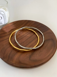 Detail of gold and silver wave texture bangles on a minimalist wooden tray display