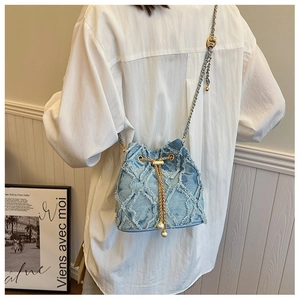 Detail of blue denim bucket bag with gold chain strap and pearl drawstring tassels