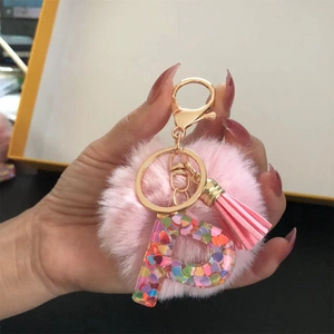 Detail of pink pompom keychain featuring a resin letter P with colorful heart sequins