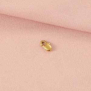 Macro detail of a 18K gold-plated stainless steel lobster clasp on pink textured fabric