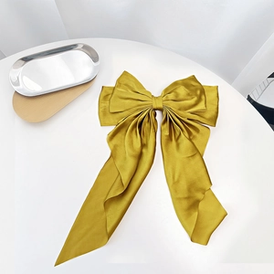 Macro detail of a golden satin bow hair clip with smooth glossy texture on white background