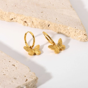 Detail of 18K gold plated butterfly earrings with hanging pearls on white stone