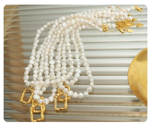 Close-up of white baroque pearl necklace with gold irregular pendant on textured glass