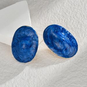 Boucles d'oreilles ovales dorées avec émail marbré bleu sur fond de pierre blanche