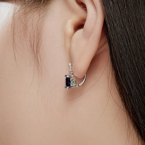 Close-up of deep blue square-cut zircon earrings set in polished silver on a female model