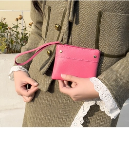 Pink lychee grain leather coin purse with gold studs and wrist strap held by hand