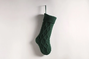 Detailed close-up of a green knitted Christmas stocking with diamond pattern on white wall
