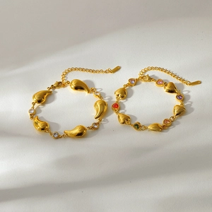 Détail du bracelet en acier doré avec charms en zircon coloré en forme de cœur et de feuille
