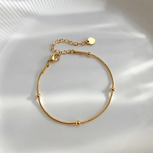 Elegant gold snake chain bracelet with small beads and heart charm on a textured tray