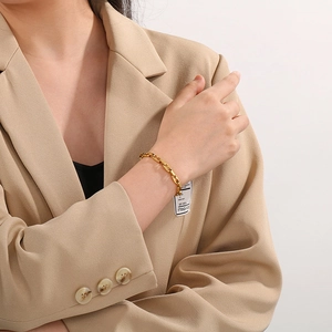 Detailansicht eines goldfarbenen Gliederkettenarmbands am Handgelenk mit weißem Anhänger
