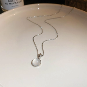 Minimalist silver necklace featuring a round cat-eye stone pendant on a white ceramic plate