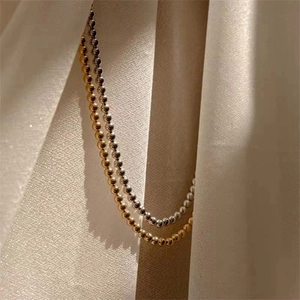 Close-up of polished gold and silver bead necklaces on textured beige fabric with soft lighting