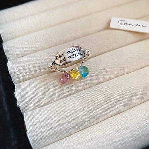 Macro shot of silver oval ring engraved with Latin text and three colorful zircon charms