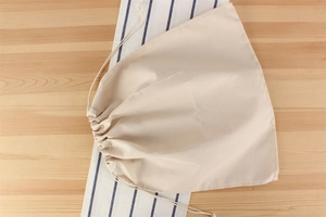Detail of beige cotton-linen drawstring pouch on a striped fabric background