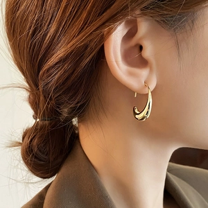 Macro detail of high-polish gold teardrop earrings showing the smooth metal finish